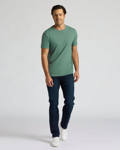 True ClassicA man modeling a sage green crew-neck t-shirt, dark blue jeans, and white sneakers against a light gray studio background.