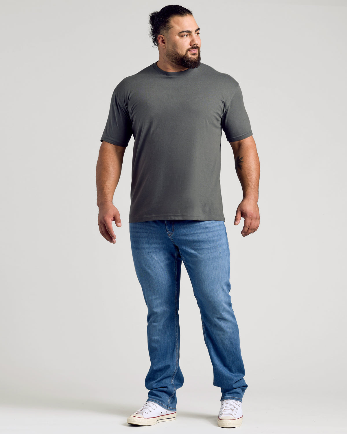 Man in Carbon Classic Crew Neck, relaxed stance, showcasing tattooed forearm.