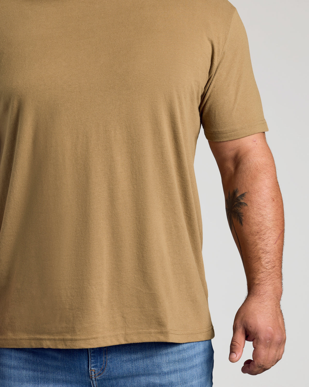 Tan 499 Classic Crew Neck with palm-tree tattoo on forearm.