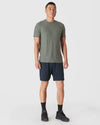 Man wearing Heather Forest Short Sleeve Active Crew Neck, navy shorts, black sneakers.