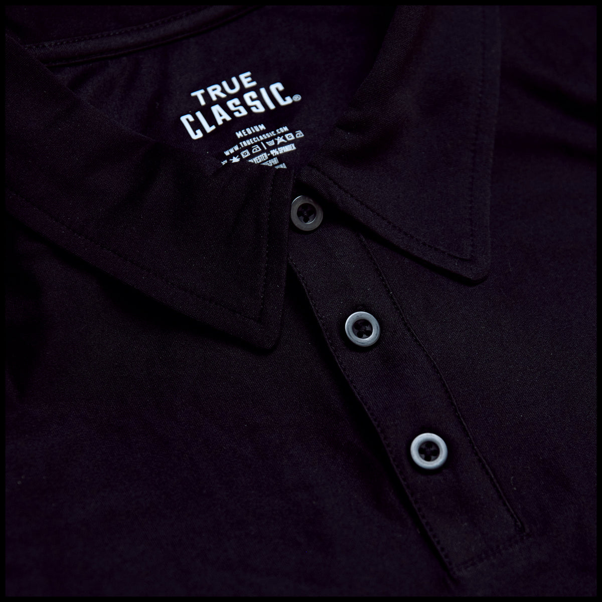 Black Active Polo 2.0 close-up, featuring collar, three-button placket, TRUE CLASSIC label.