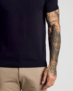 True ClassicBlack Short Sleeve Sweater Polo on tattooed arm, tucked into khaki pants.