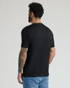 Man wearing black crew neck t-shirt from the Black & White Pima Cotton Blend Crew 7-Pack, shown from the back with tattoos visible on arm, paired with light blue jeans.
