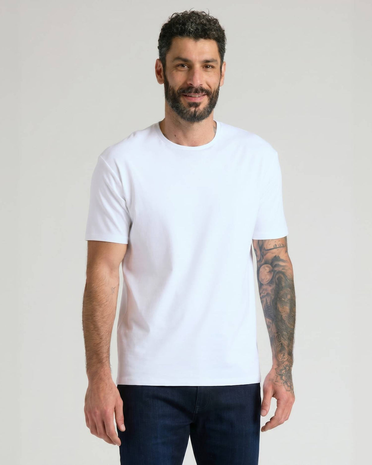 Man wearing a plain white crew neck t-shirt and dark jeans, showcasing the Pima Cotton Blend Crew 7-Pack as a comfortable men's basics essential.