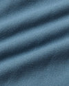 A close-up of textured blue fabric with soft diagonal folds and a fine woven pattern.