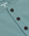 Close-up of a blue knit Henley shirt featuring dark buttons and visible stitching, part of the Heavyweight Curved Hem Henley 3-Pack by True Classic, a men's basics essential.