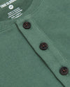 Close-up of a green Neo Fern Heavyweight Curved Hem Henley featuring a textured knit fabric and three dark buttons along the placket, highlighting men's basics.