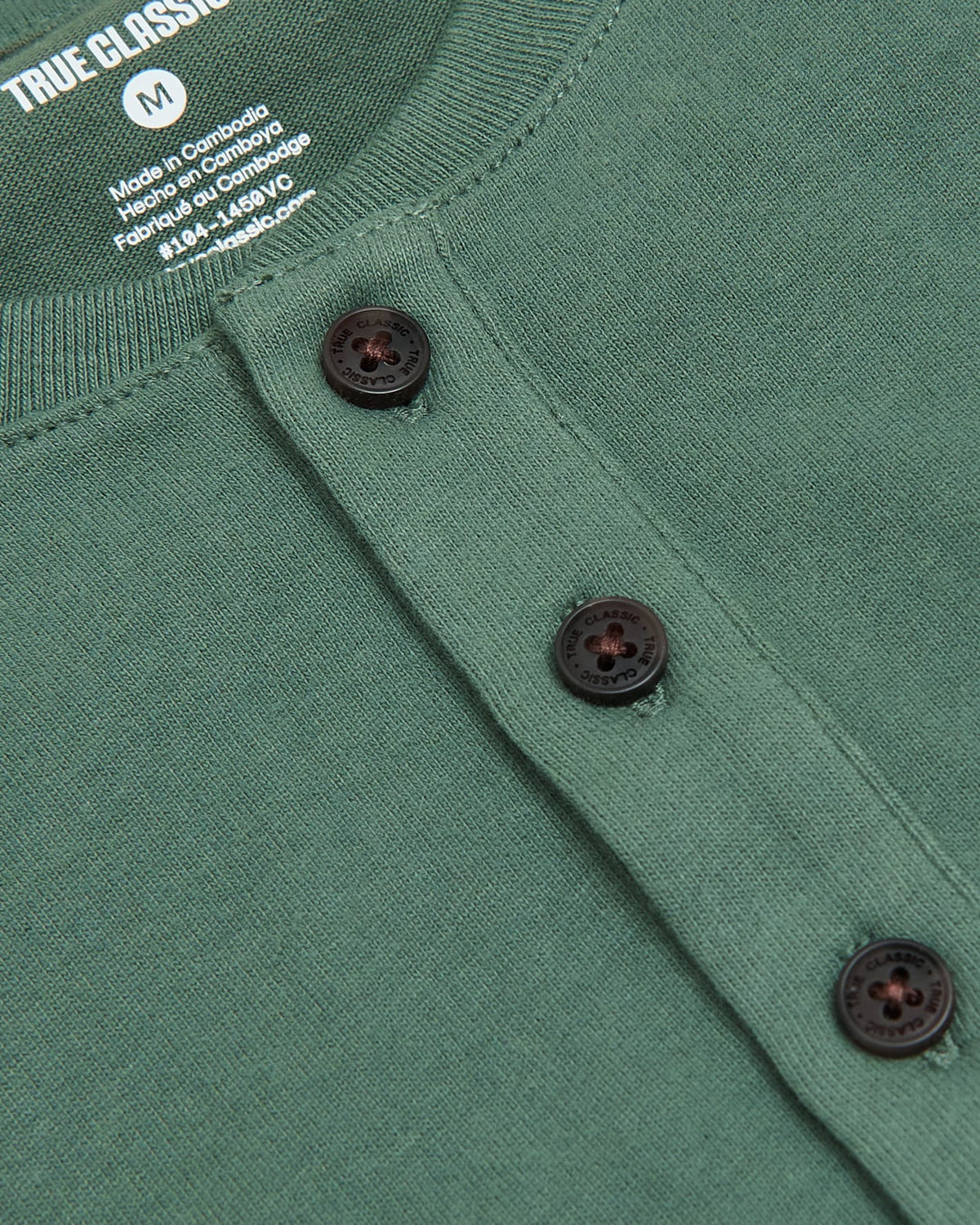 Close-up of a green Neo Fern Heavyweight Curved Hem Henley featuring a textured knit fabric and three dark buttons along the placket, highlighting men's basics.
