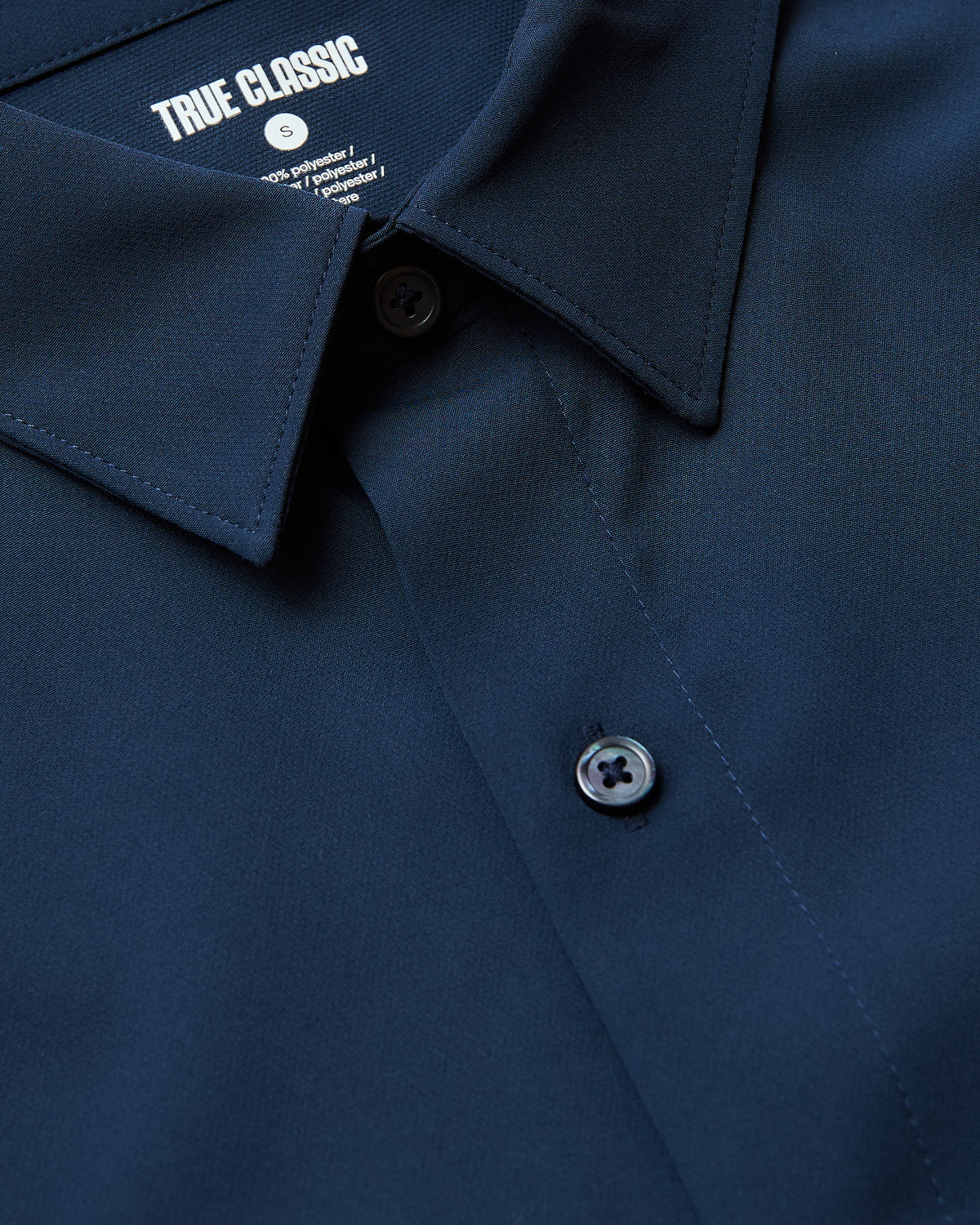 Close-up of a navy blue Navy Performance Long Sleeve Dress Shirt highlighting its smooth fabric, button details, and classic collar design from True Classic’s men's basics collection.