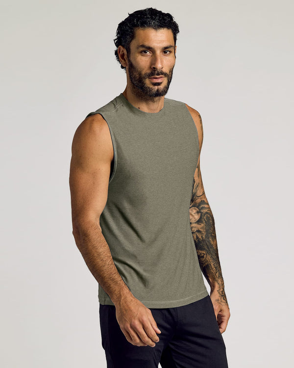 Man wearing a Heather Military Green Sleeveless Active Muscle Tee with a fit build and tattooed arm, posing confidently against a plain background in men's basics style.