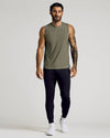Man wearing a Heather Military Green Sleeveless Active Muscle Tee paired with black joggers and white sneakers, showcasing a casual and athletic men's basics look.
