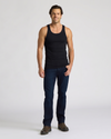 Man wearing a black tank top and dark blue jeans on a white background