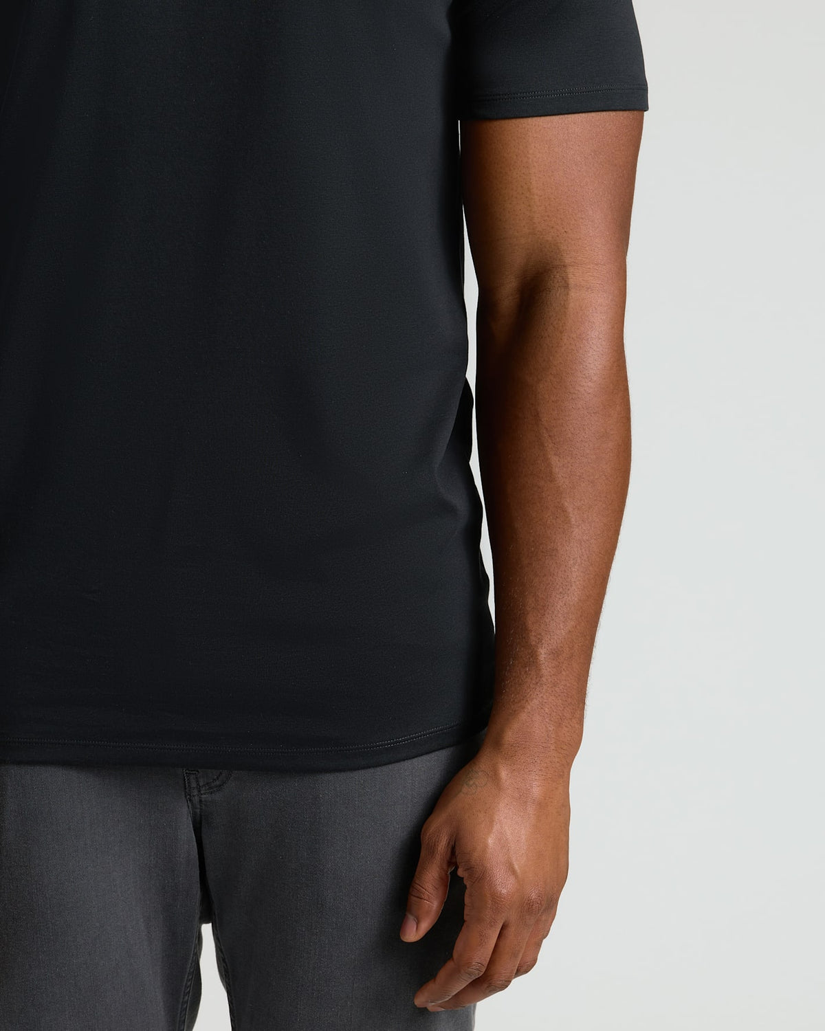 Close-up of a man wearing a black crew neck t-shirt paired with dark gray jeans, showcasing the fit and texture of the Tall Pima Cotton Blend Crew 7-Pack men's basics.