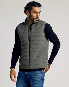 True ClassicMan wearing a gray Carbon Puffer Vest over a black long-sleeve shirt and blue jeans, showcasing a casual and comfortable men's basics look.