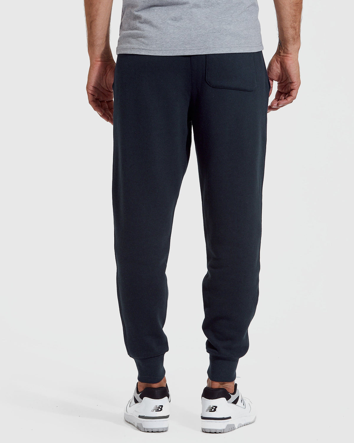 Rear view of a man wearing navy jogger pants paired with white sneakers, part of the Navy Pullover Fleece Hoodie & Jogger 2-Pack, showcasing comfortable men's basics.