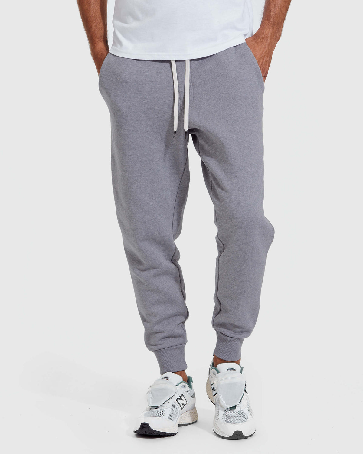 Front view of a person wearing Heather Gray Fleece French Terry Joggers with a white drawstring, paired with white athletic sneakers, showcasing a casual men's basics style.