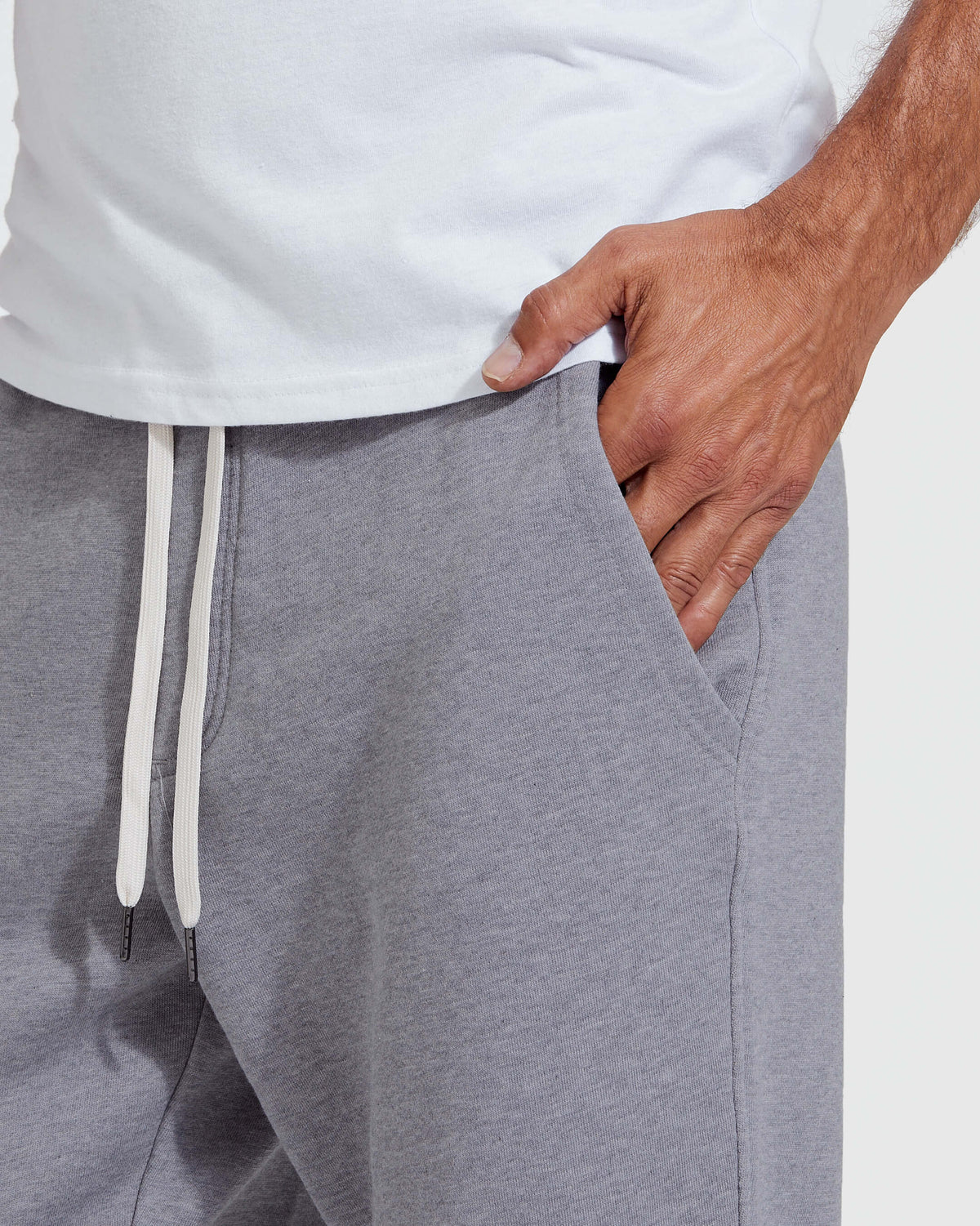 Man wearing Heather Gray Fleece French Terry Joggers with hand in pocket, showing soft fabric texture and white drawstrings on waistband.