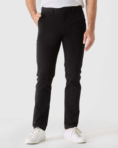 True ClassicBlack Slim Twill Chino Pant with white sneakers in a studio setting.