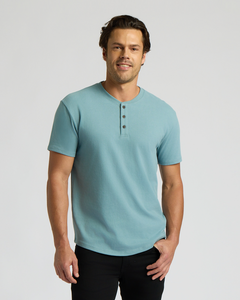 True ClassicMan wearing a light blue Heavyweight Curved Hem Henley 3-Pack shirt with short sleeves and three buttons, styled with casual black pants against a plain background.