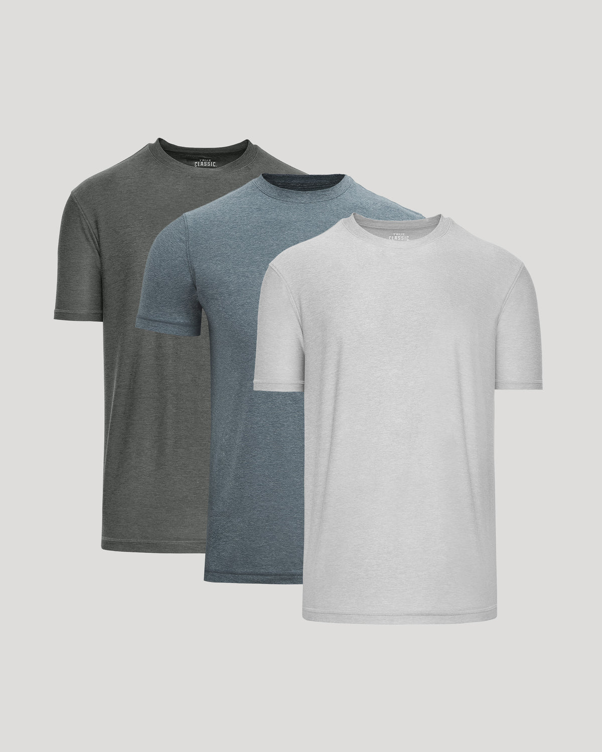 Three short-sleeve crew-neck t-shirts in dark gray, heather blue, and white, arranged in a layered overlapping display against a solid light gray background.
