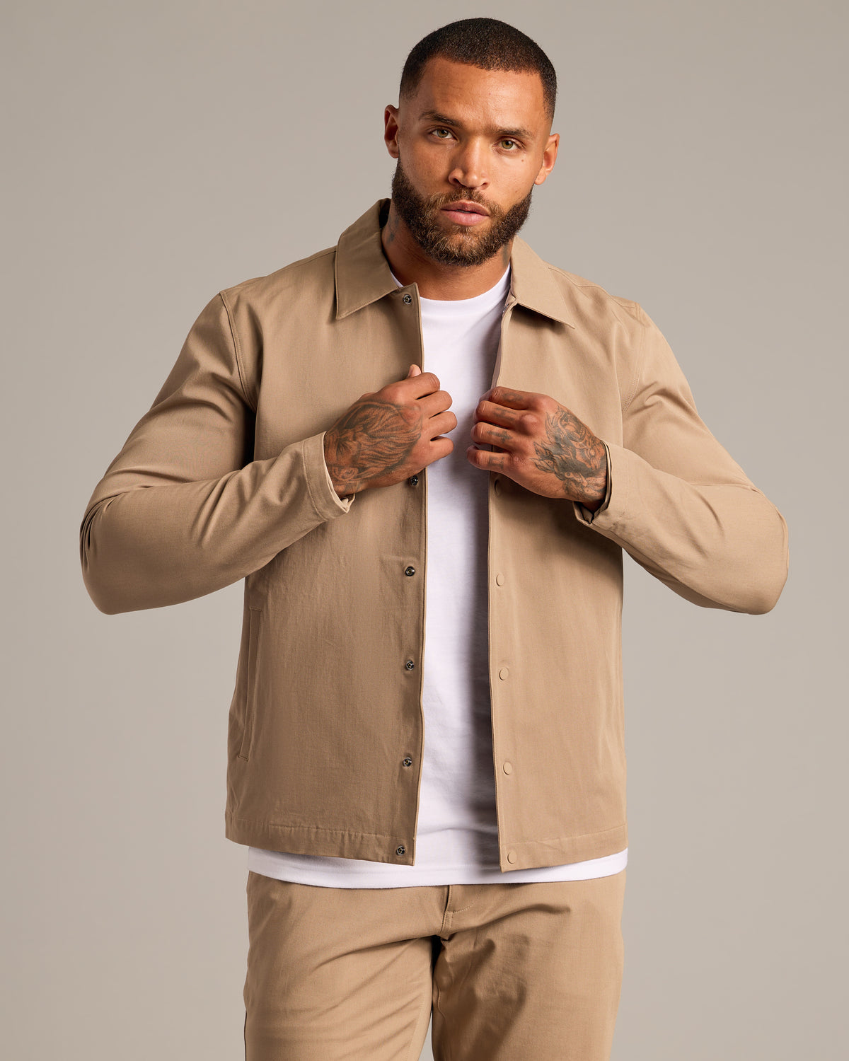 Man wearing Khaki Coaches Jacket, adjusting it against a plain backdrop.