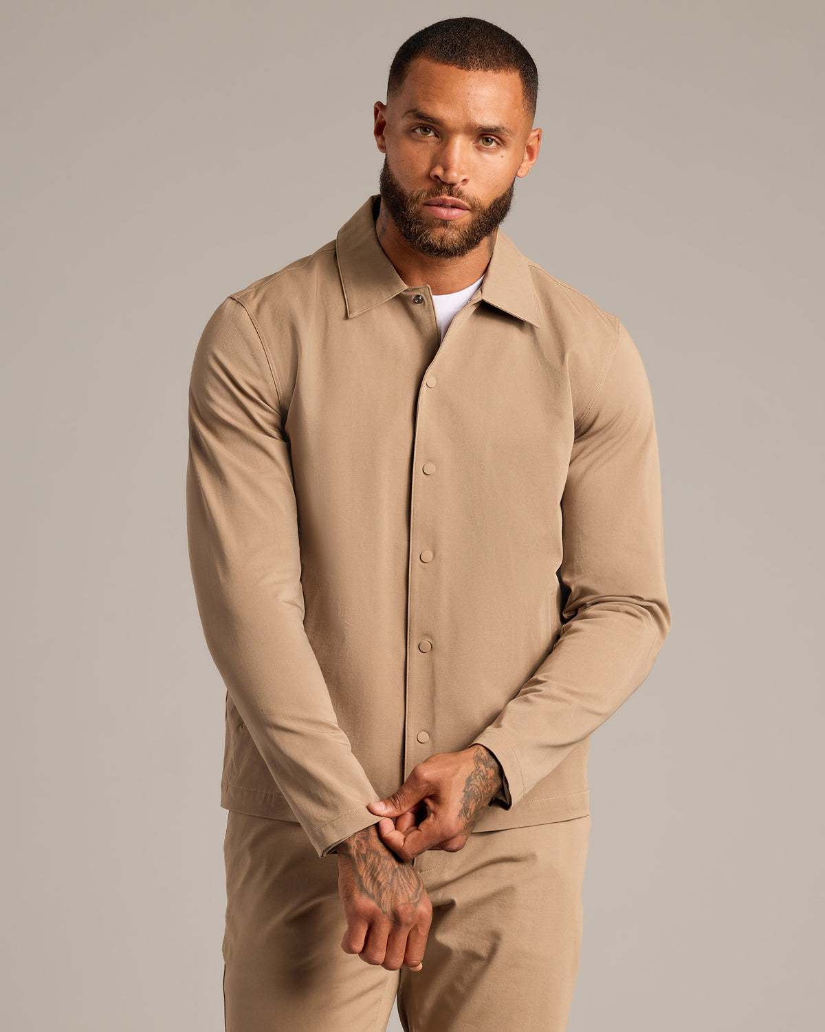 Model in Khaki Coaches Jacket adjusting cuff, showcasing tattoos.