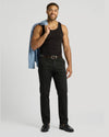 A smiling man wearing a black Ribbed Curved Hem Tank 3-Pack top paired with black pants, holding a light blue jacket over his shoulder, showcasing casual men's basics style.