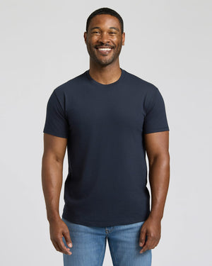 Man wearing a navy blue t-shirt and blue jeans against a plain background. 
