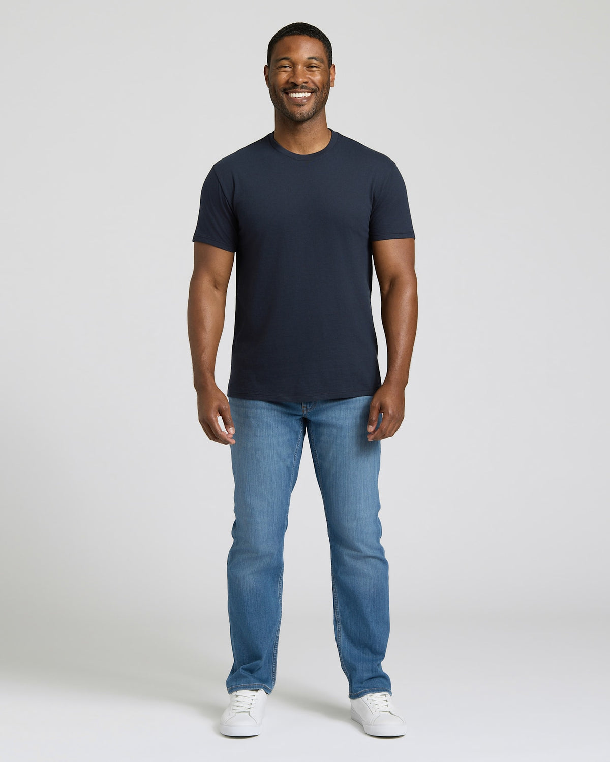 Man wearing a navy t-shirt and blue jeans on a white background. MODEL_INFO: Model is 5'8" wearing size M short
