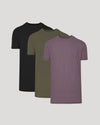 Three short-sleeve crew-neck t-shirts in black, olive green, and heathered dusty purple, arranged in a staggered overlapping layout on a light gray background.
