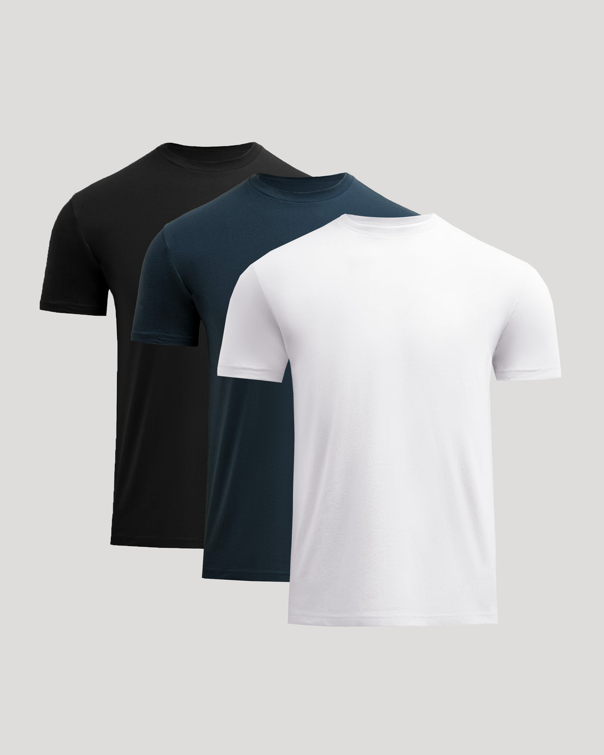 Three plain t-shirts in black, navy, and white on a light gray background