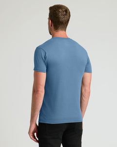 True ClassicA man viewed from the back wearing a solid medium blue short-sleeve crewneck t-shirt and black pants, set against a plain light gray studio background.