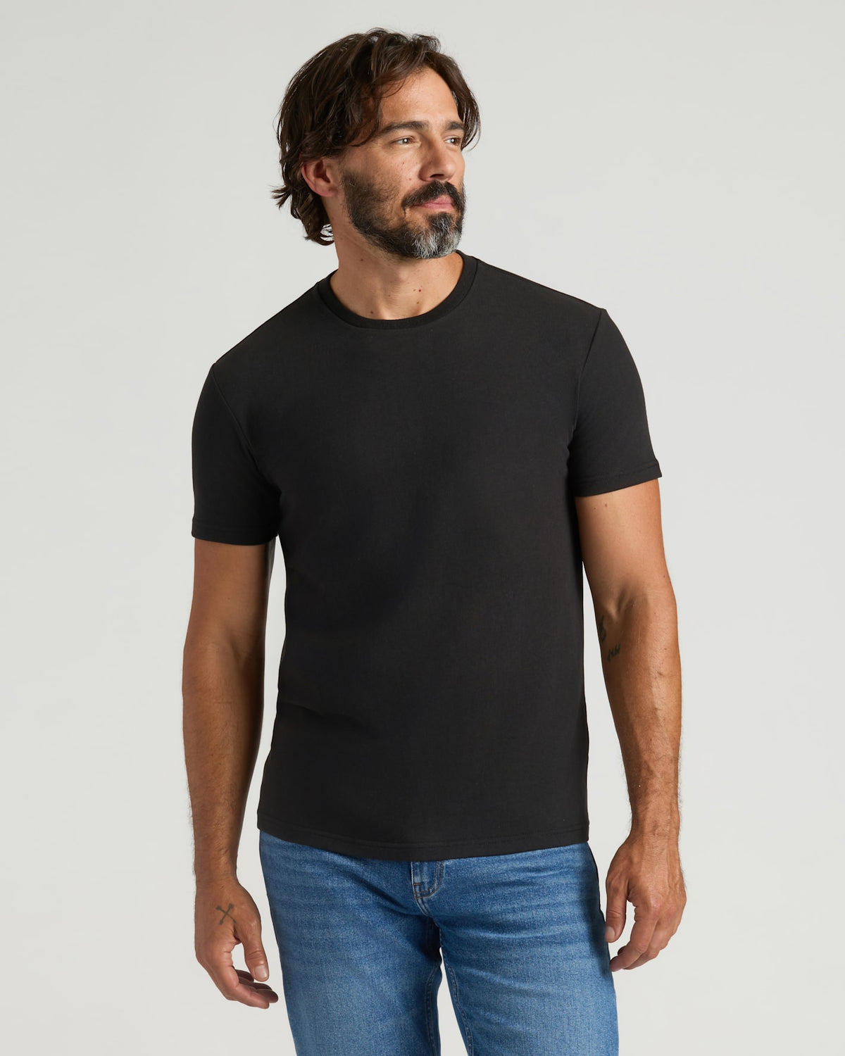 Man wearing a black t-shirt and blue jeans against a plain background