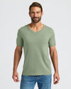 Man wearing a green t-shirt and blue jeans on a light gray background