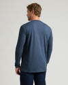 A man viewed from the back wearing a heathered slate blue long-sleeve t-shirt and dark blue jeans, standing against a light gray studio background.