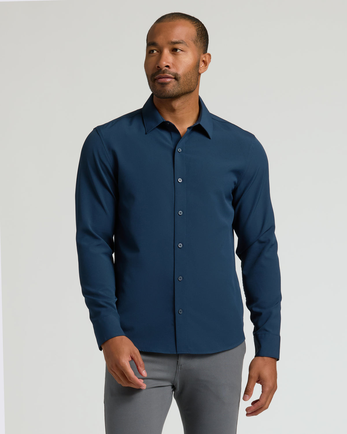 Man wearing a fitted Navy Performance Long Sleeve Dress Shirt with button front and collar, styled with gray pants against a plain light background.