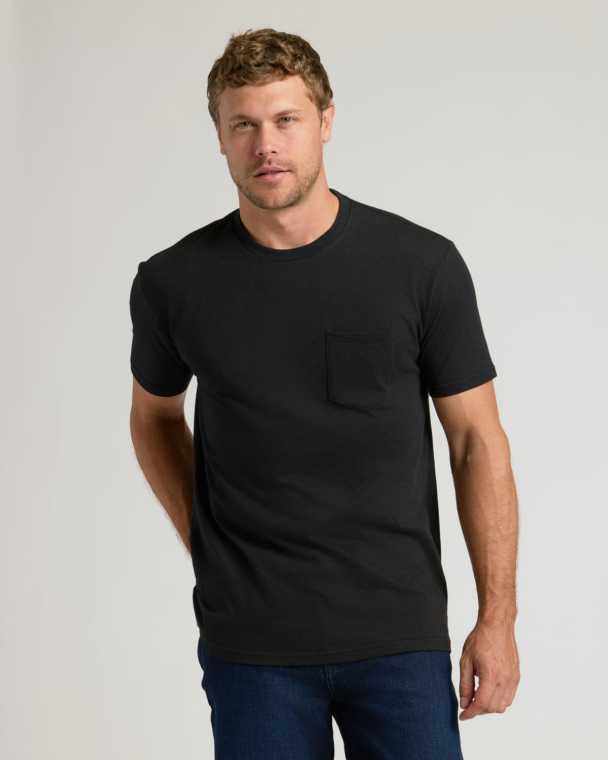 Male model wearing a black classic pocket crew t-shirt, part of the Classic Pocket Crew 6-Pack, paired with dark blue jeans against a plain background.