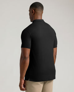 True ClassicA man viewed from the back wearing a black short-sleeve polo shirt and beige trousers, photographed against a plain light gray studio background.
