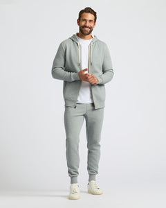 True ClassicA man modeling a light gray two-piece tracksuit featuring a zip-up hoodie with white drawstrings and matching jogger pants, styled over a white t-shirt and cream sneakers against a light gray studio background.