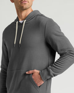 True ClassicA man wearing a dark gray pullover hoodie with cream-colored drawstrings, shown from the chest up against a light gray studio background.