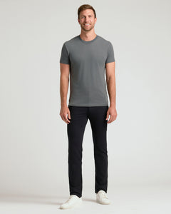 True ClassicA man modeling a short-sleeve crewneck t-shirt in dark gray, paired with black pants and white sneakers, standing against a light gray studio background.