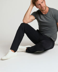 True ClassicA man sitting on a light gray floor wearing a gray crewneck t-shirt, slim black trousers, and white sneakers.