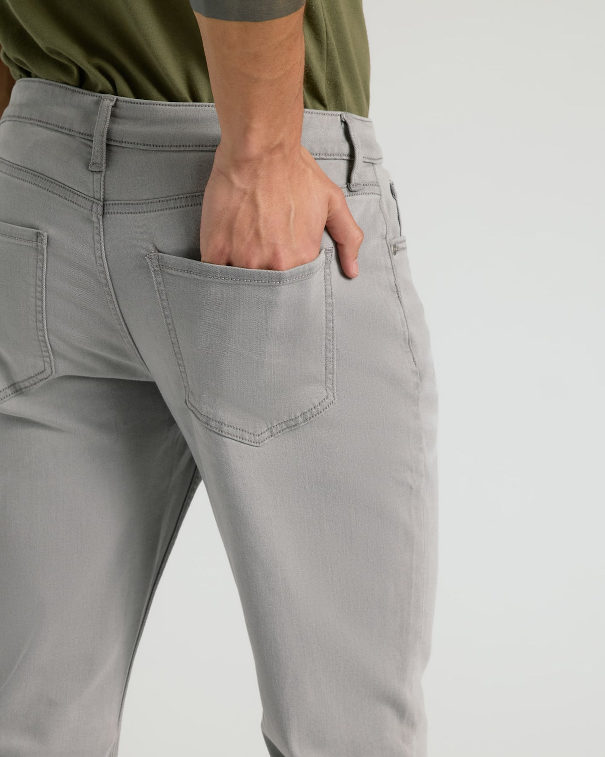 Close-up of a person wearing light gray slim-fit jeans, with the hand tucked into the back pocket, against a plain light gray background.