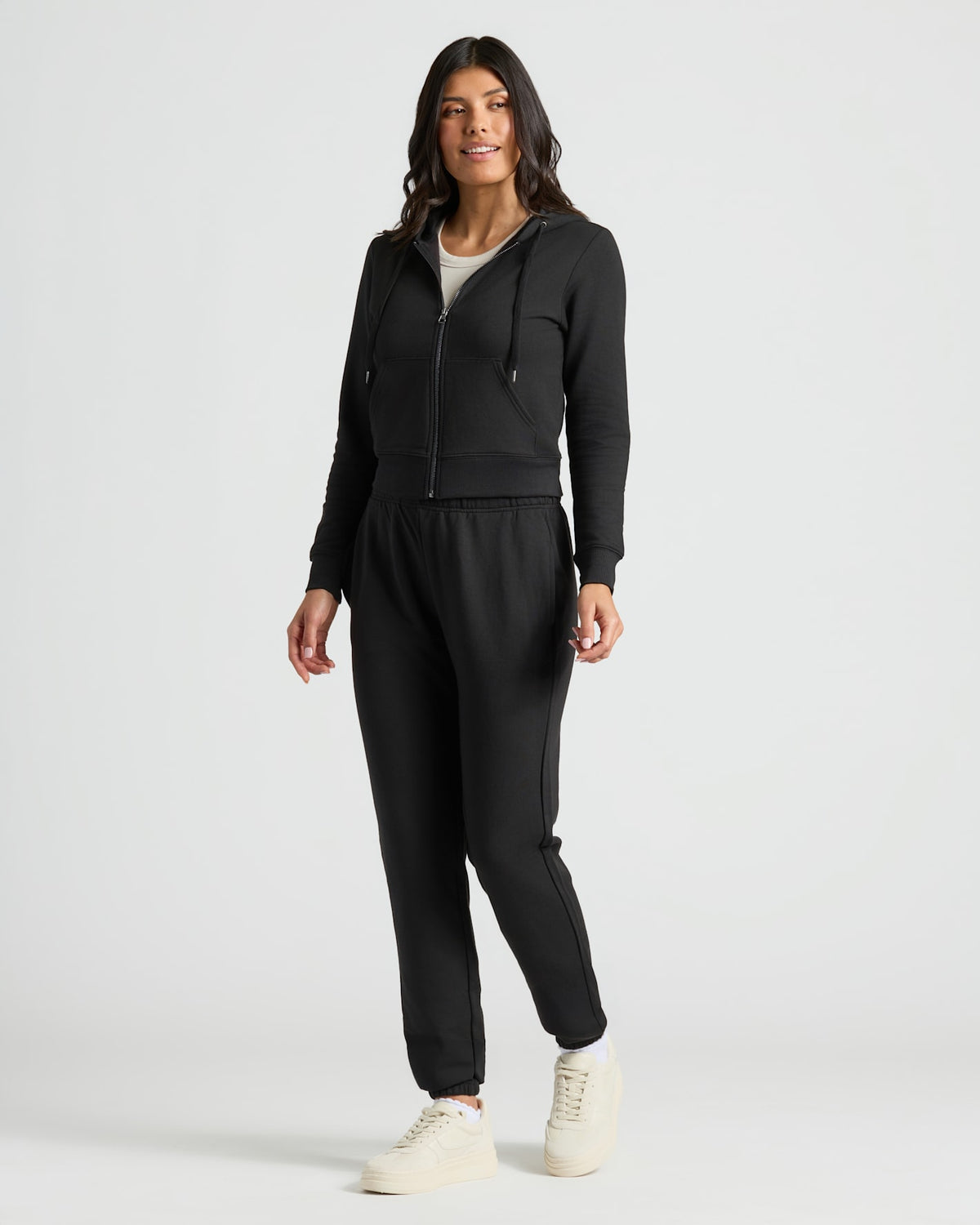 Woman wearing a black tracksuit with white sneakers on a light gray background