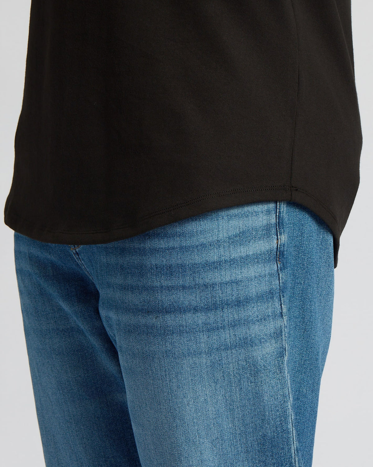Close-up of a person wearing the Black Tall Heavyweight Curved Hem Crew paired with blue jeans, highlighting the curved hem detail on men's basics.