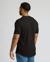 Man wearing an All Black Tall Heavyweight Curved Hem Crew 3-Pack t-shirt, shown from the back, paired with blue jeans against a plain light gray background.