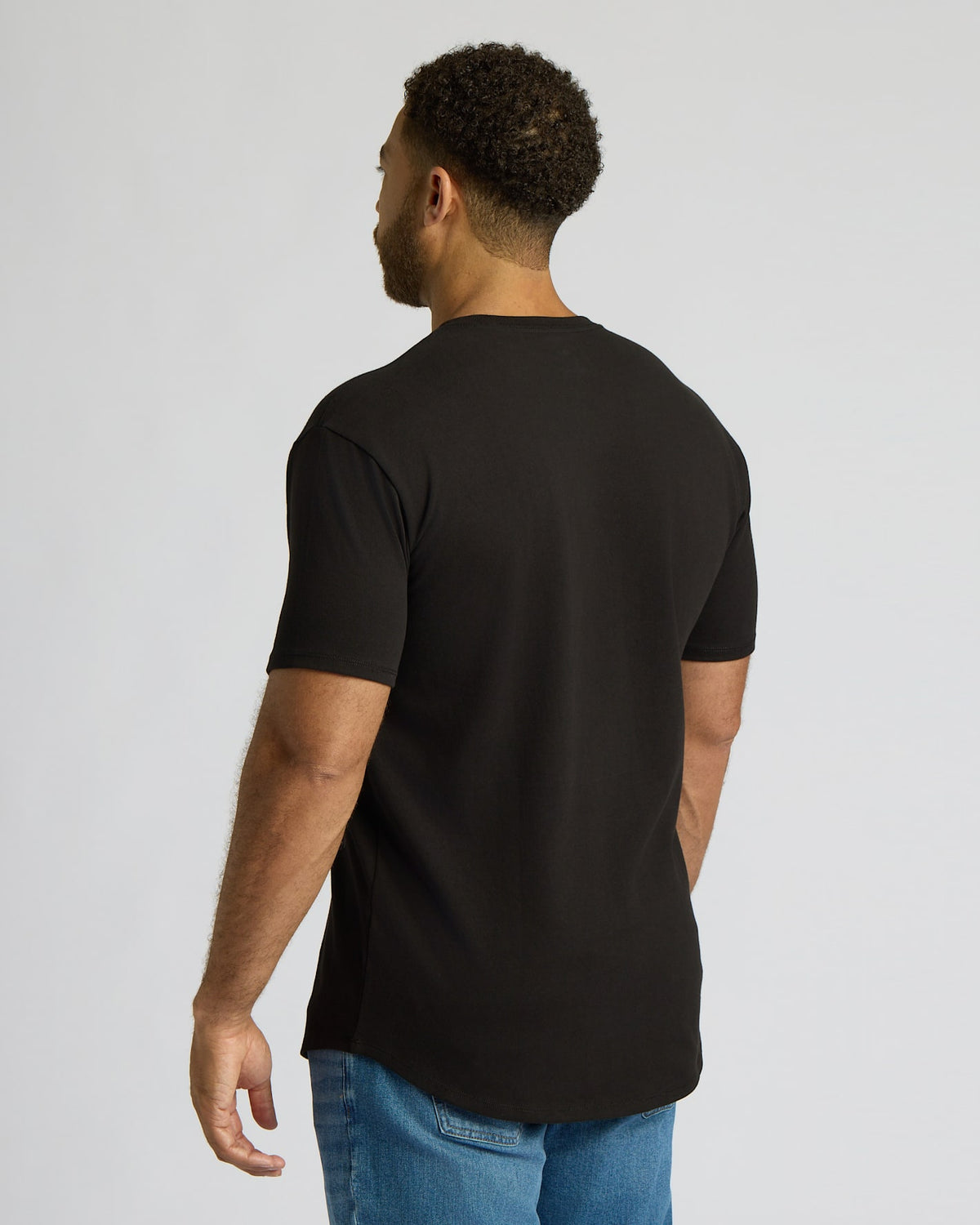 Man wearing an All Black Tall Heavyweight Curved Hem Crew 3-Pack t-shirt, shown from the back, paired with blue jeans against a plain light gray background.