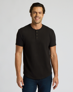 True ClassicMan wearing a black Heavyweight Curved Hem Henley 3-Pack shirt with short sleeves and buttoned placket, paired with dark blue jeans, smiling against a plain background.