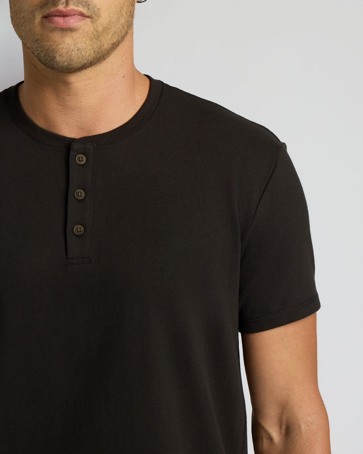 Close-up of a man wearing an All Black Heavyweight Curved Hem Henley 3-Pack shirt, featuring a three-button placket and short sleeves in a men's basics style.