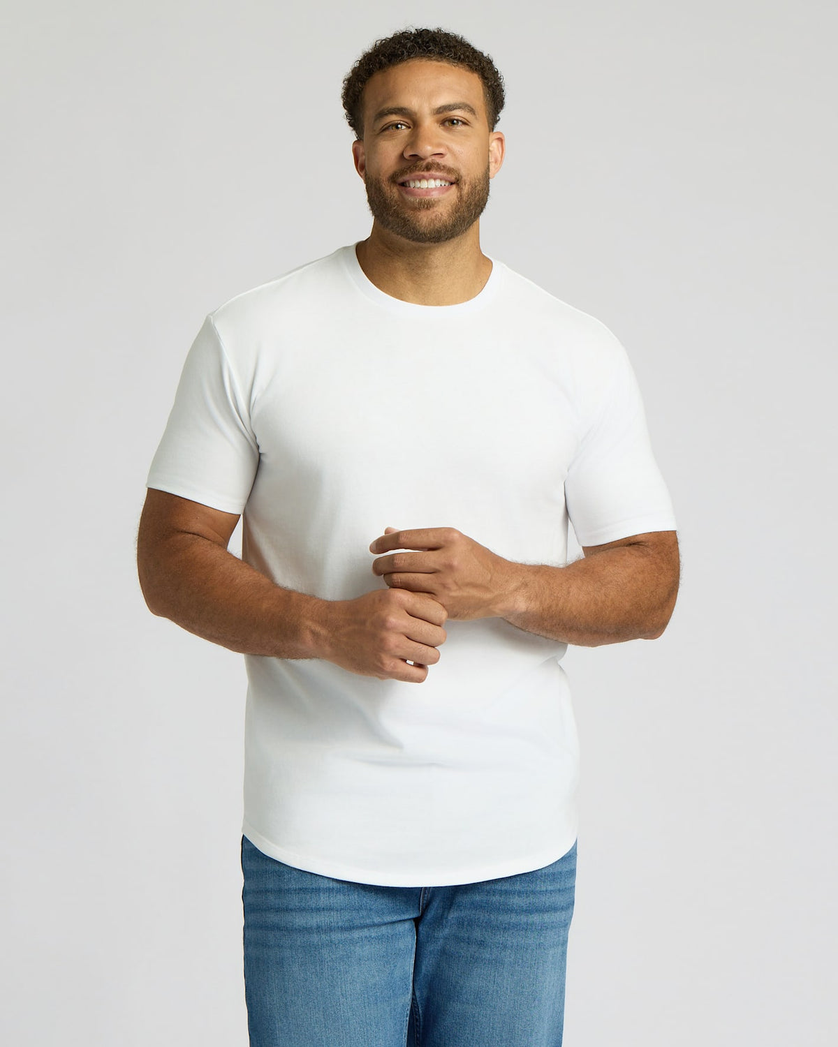 Smiling man wearing an All White Tall Heavyweight Curved Hem Crew 3-Pack t-shirt paired with blue jeans, showcasing a classic men's basics style.